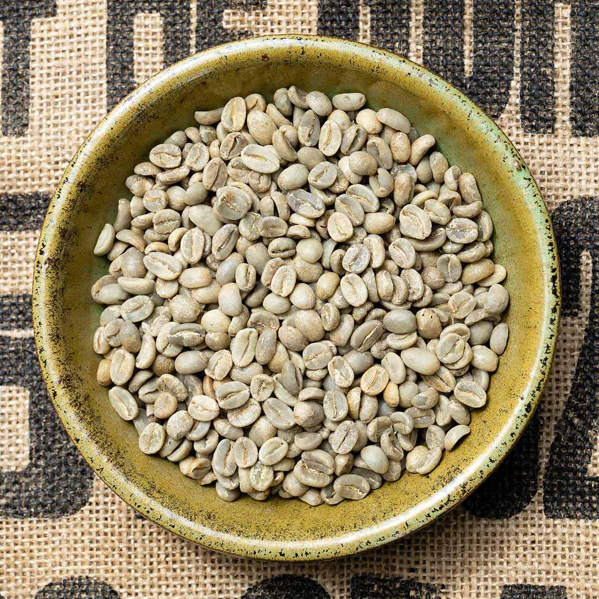 raw green coffee beans in a bowl atop a burlap bag